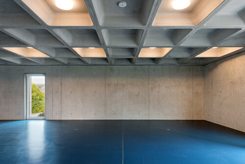 Sichtbetonwände im Inneren der Gebäude, tiefblauber Fußboden, Decke aus Rasterelementen und Beleuchtung