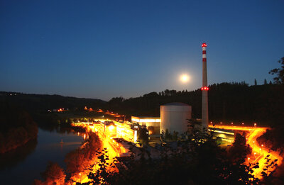 Das Schweizer Kernkraftwerk Mühleberg bei Nacht mit Beleuchtung entlang der Grundtstücksgrenze, Mond im Hintergrund