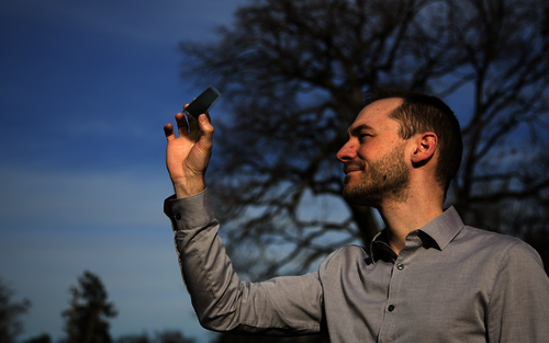 Ein junger Mann hält an freier Luft eine semitransparente organische Solarzelle in der rechten Hand ins Tageslicht