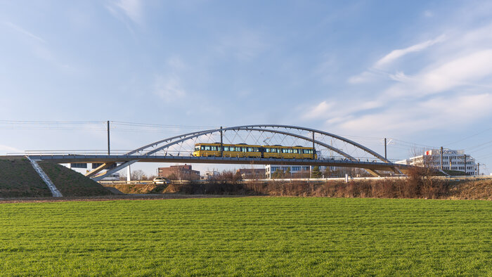 Deutscher Ingenieurbaupreis 2022: Stadtbahnbrücke Stuttgart Degerloch, Aufnahme bei Sonnenschein, Bogen-Brücke vor blauem Himmel, im Vordergrund Wiese