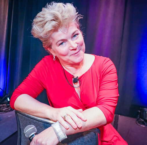 Kommunikationsexpertin Katja Schleicher in rotem Obertal, Kopf schräg haltend, Arme locker über den Sessen verschränkt