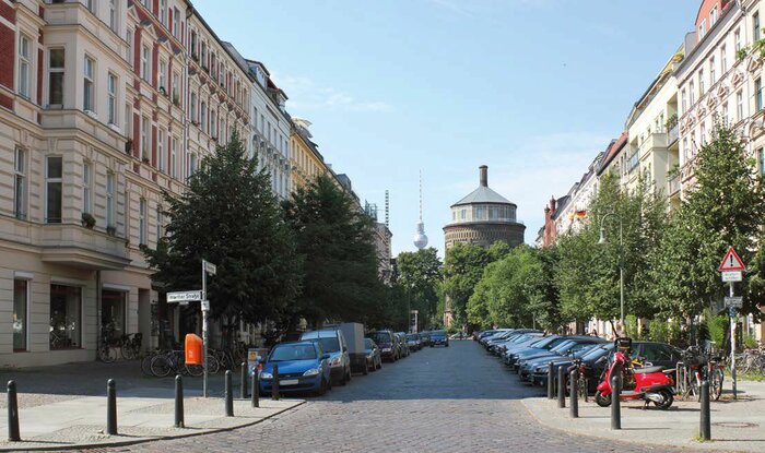 Ein Beispiel für eine grüne Wohnstraße (im Bild eine Straße am Prenzlauer Berg in Berlin). Bäume verschatten im Sommer Teile der Straße, die klare Trennung der Fahrbahn von den Stellplätzen und dem grünen Seitenraum verringern das Konfliktpotenzial zwischen den Verkehrsteilnehmern. Grüne Straßenräume bieten eine hohe Aufenthaltsqualität.