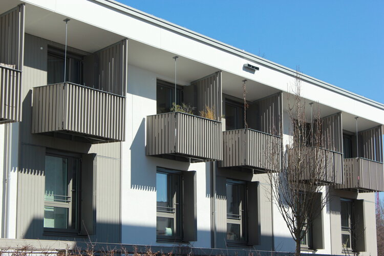 Graues Mehrfamilienhaus in Kubusform mit fünf vorgesetzten Balkonen im Ausschnitt