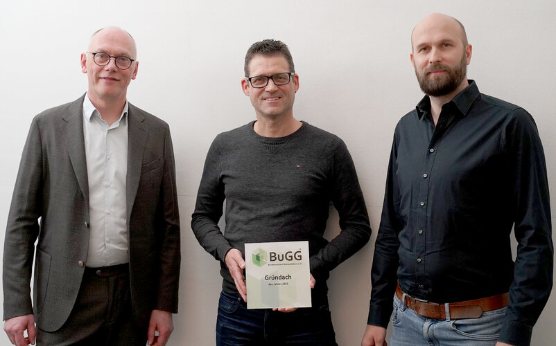BuGG-Präsident Dr. Gunter Mann (Mitte) überreicht den Geschäftsführern von Landschaftsarchitektur+ Felix Holzapfel-Herziger (links) und Julian Benesch (rechts) die Siegerplakette zum BuGG-Gründachdes Jahres 2021.