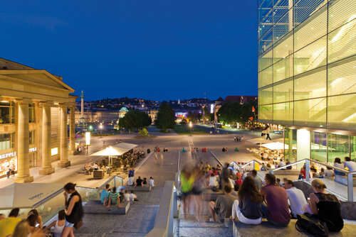 Treppe, Kleiner Schlossplatz, Kunstmuseum, Schlossplatz, Stuttgart: blauer Himmer, goldfarben beleuchtete Gebäude am Abend, Menschen sitzen auf Treppenstufen