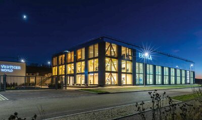 Das Gebäudeensemble der Envola GmbH besteht aus einer Produktionshalle und einem Bürotrakt, die in einem kompakten Quader zusammengefasst sind. Die Fassadengestaltung ermöglicht die Unterscheidung beider Bereiche von außen, vereint sie aber dennoch zu einem lebendigen Ganzen.