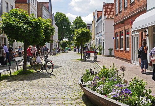 Innenstadt von Friedrichstadt, Holländersiedlung: Gasse mit Kopfsteinpflaster, kleinen Bäumen, bepflanztem Holzkahn und flachen buntfassadigen Häusern