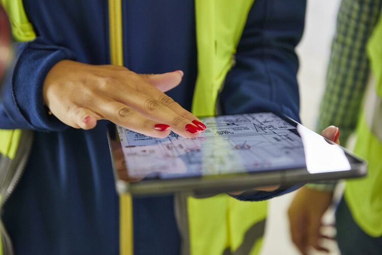 Frau mit Warnweste streicht über Touchpad zur Bearbeitung eines Bauprozesses
