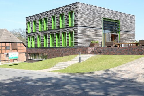 Neubau der FNR: Fassade mit Holzvertäfelung, lindgrüne Fensterrahmen, Kubusform, daneben eine Backsteingebäude mit Walmdach