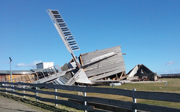 Zerstörte Bockwindmühle Klettbach Frühjahr 2022: liegend auf der Seite auf einer Wiese hinter einem Bretterzaun, blauer Himmel